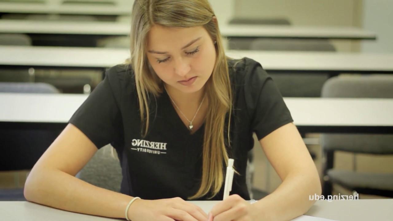 Herzing dental hygiene student in scrubs taking notes during class